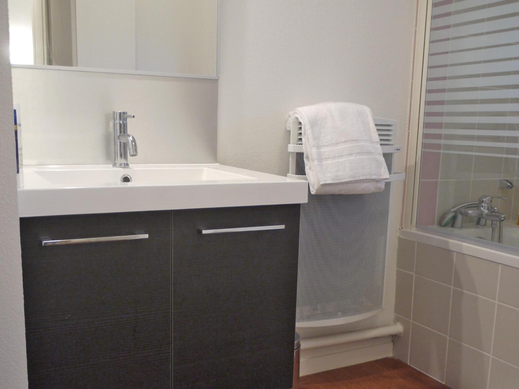 Un baño con lavamanos blanco, muebles oscuros, un perchero y una zona de ducha.