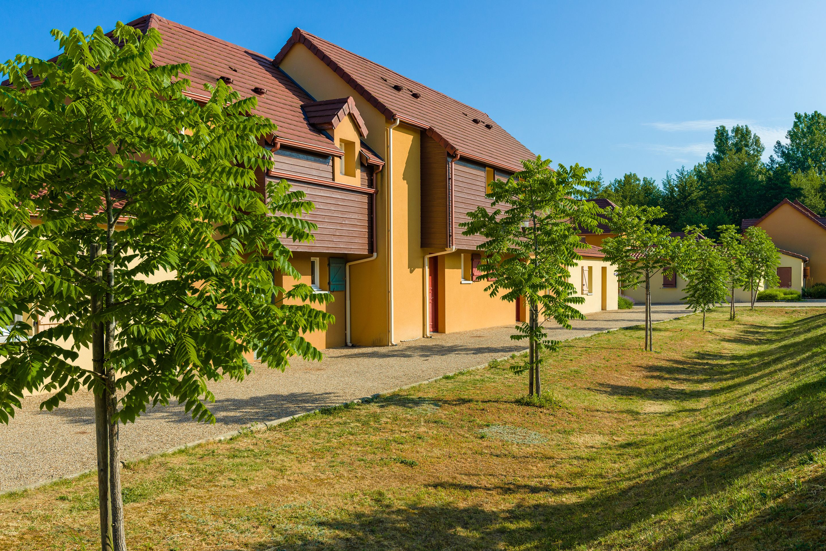 Une rangée de bâtiments jaunes aux toits bruns, entourés d’arbres verdoyants et d’une pelouse bien entretenue.