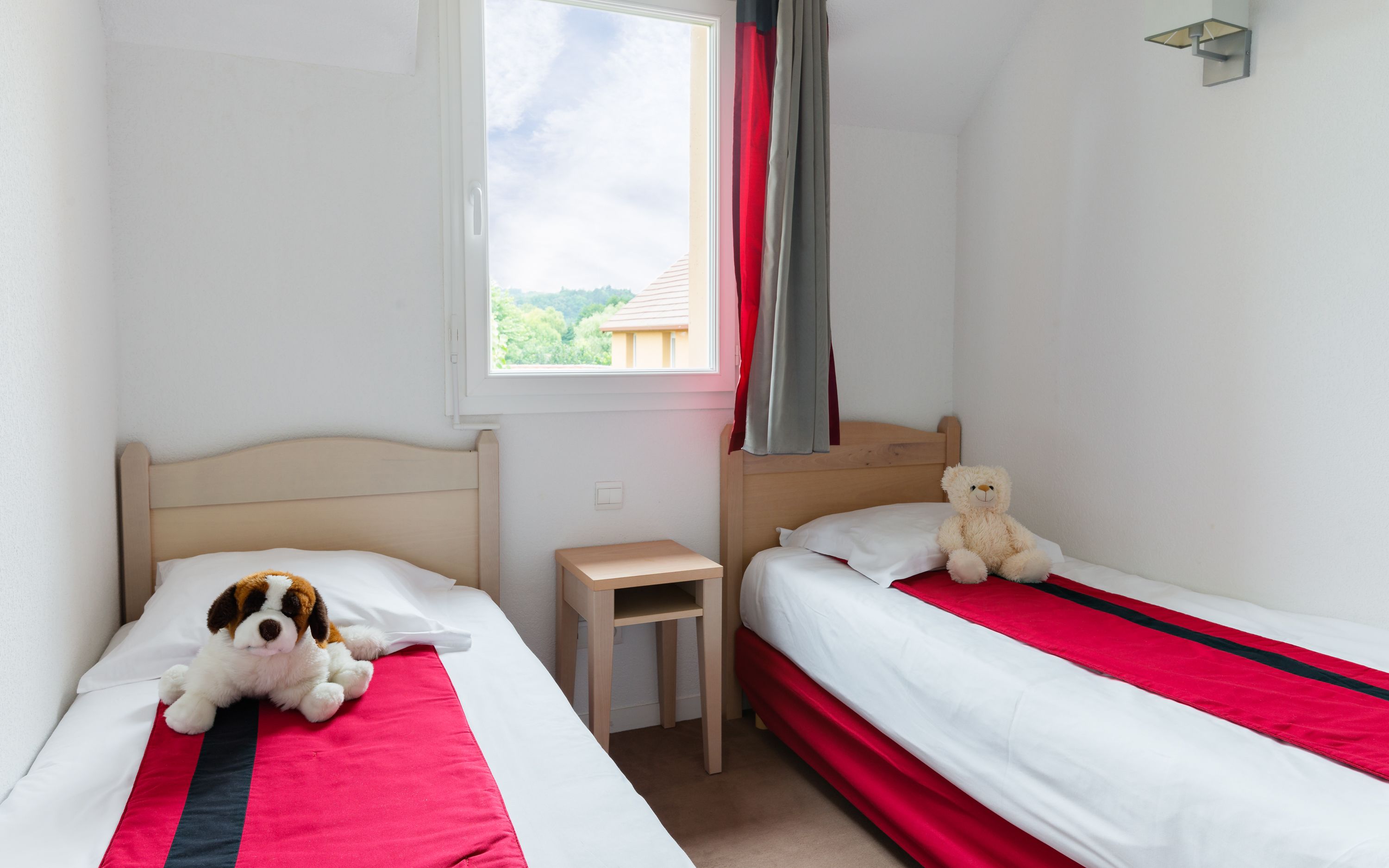 Une chambre avec deux lits, une petite table et une fenêtre avec des rideaux.
