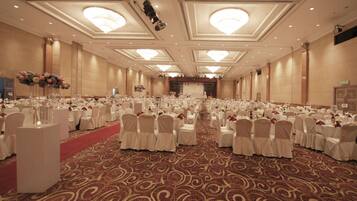 A large banquet hall with rows of round tables, white chairs, and a red carpet.