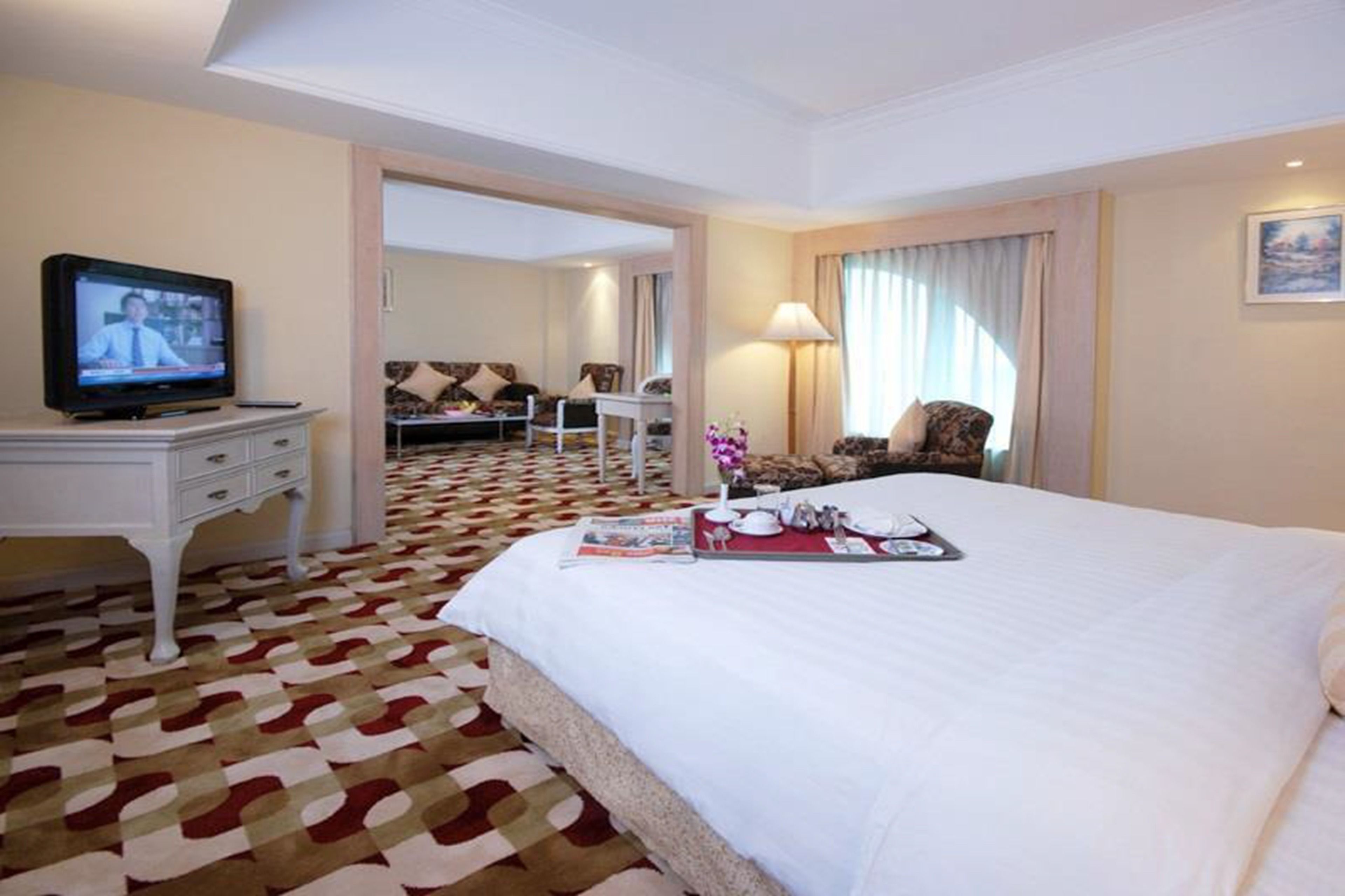 A hotel room with a large bed, a television on a nightstand, a desk, and a patterned carpet.