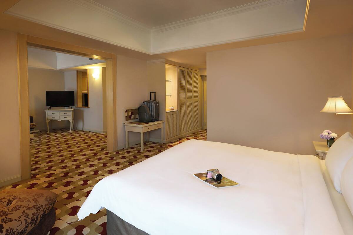 A hotel room with a large bed, a desk with a television, a wardrobe, and a patterned carpet.