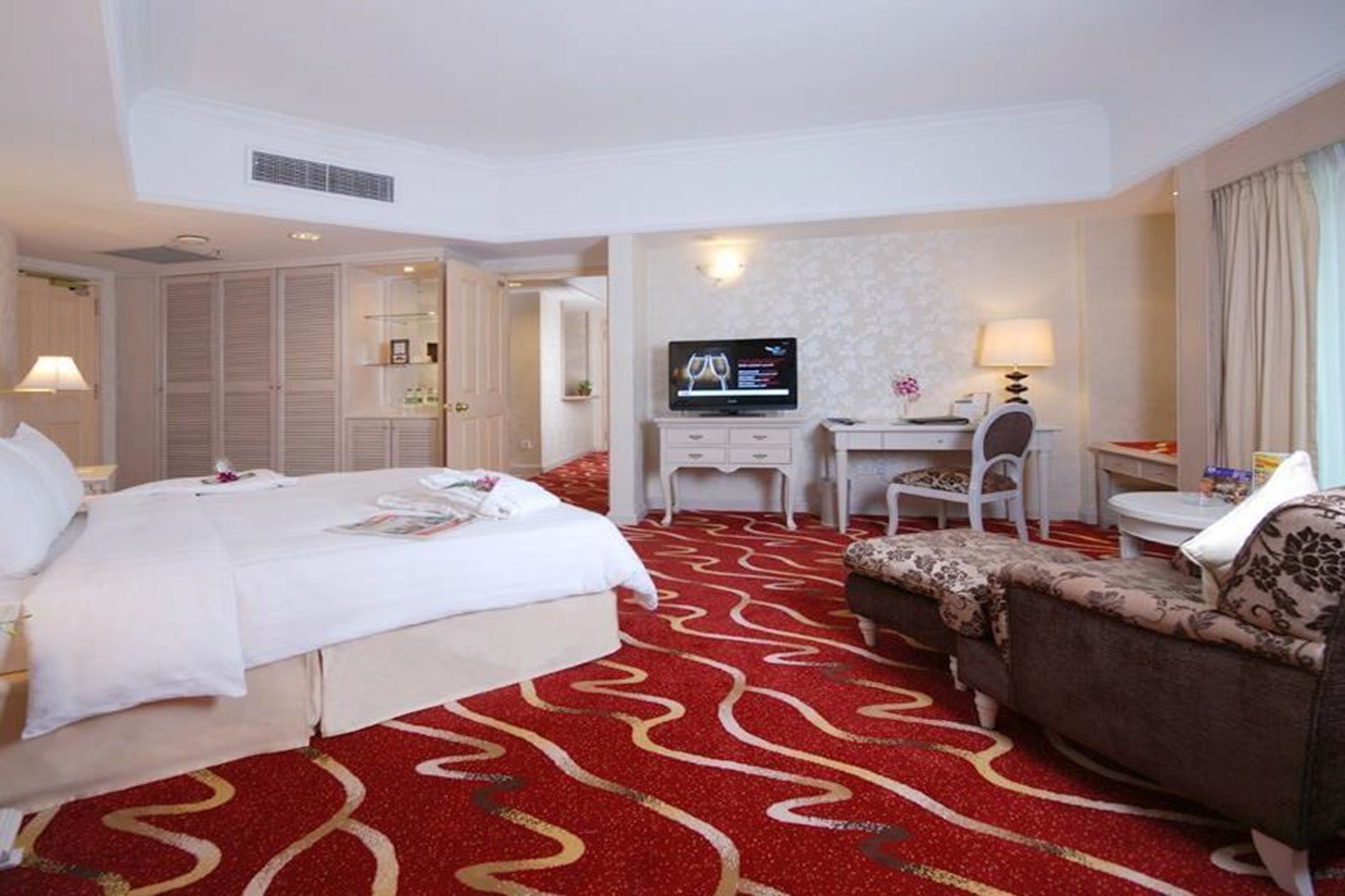 A hotel room with a large bed, a desk with a television, a chair, and a sofa.