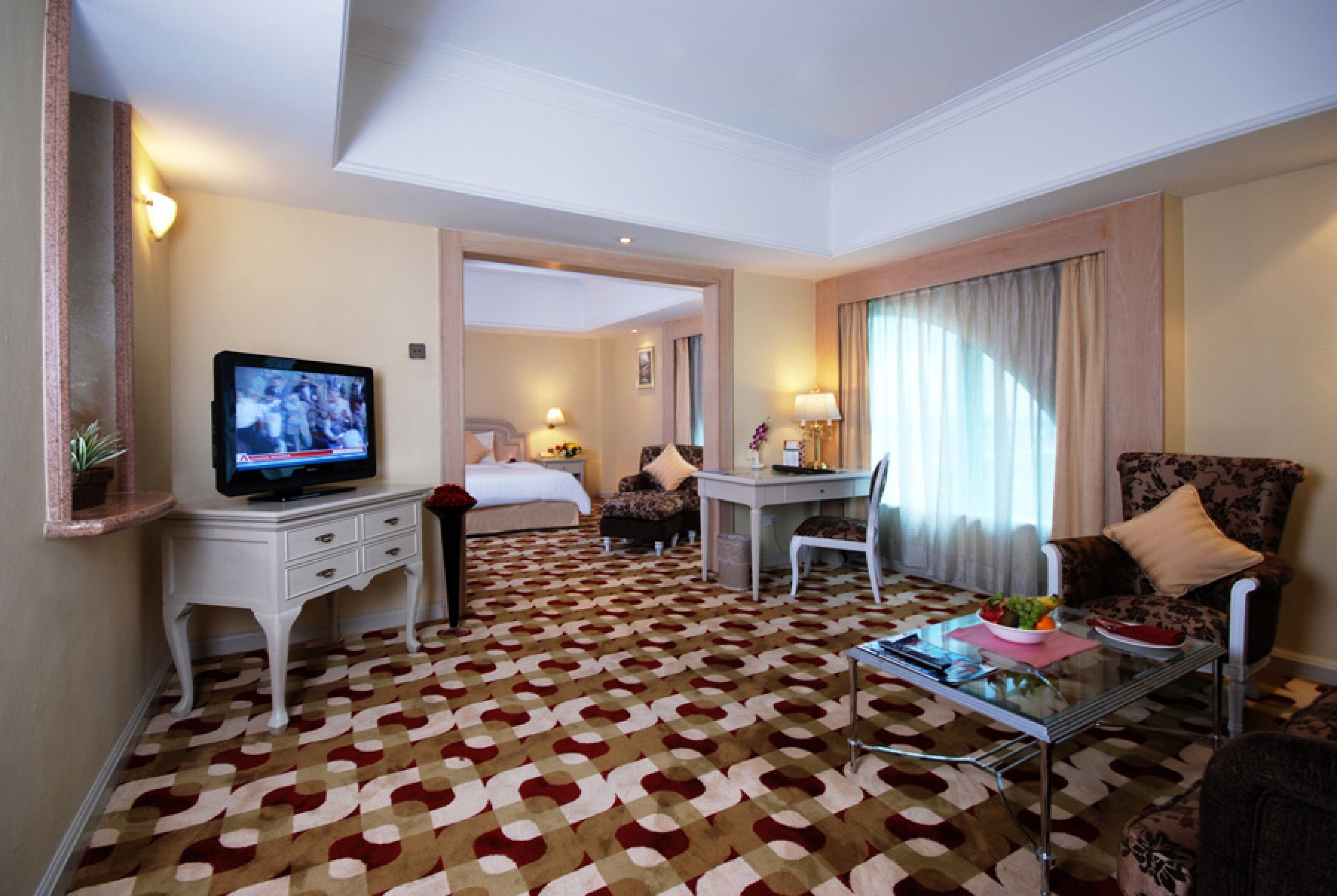 A hotel room with a bed, a desk, a television, and a seating area with a patterned carpet.