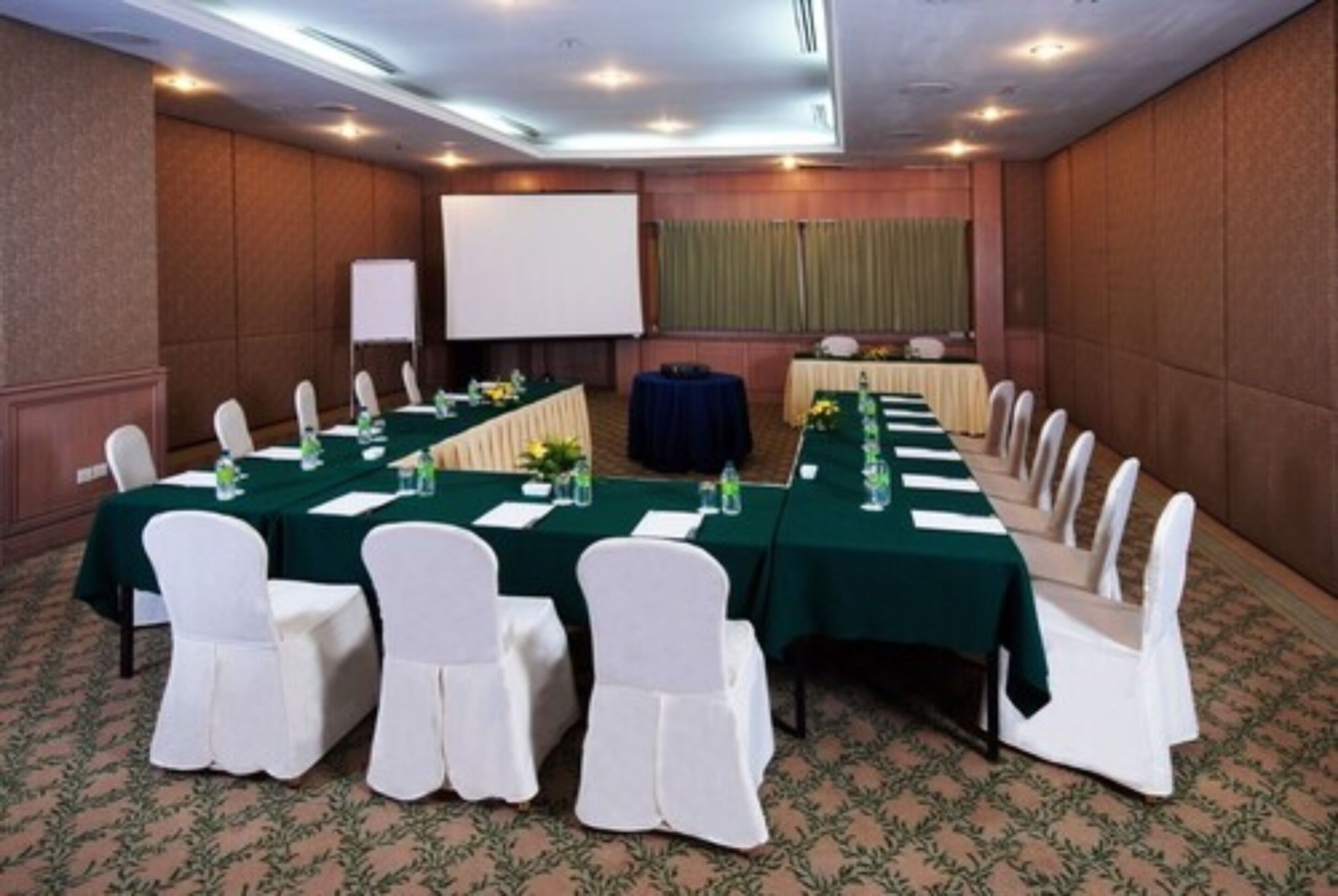 A conference room with long tables, white chairs, and a projector screen.