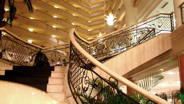 Uma escadaria imponente com grades de metal ricamente decoradas e uma série de luzes de teto iluminadas.