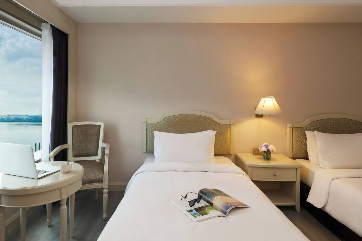 A hotel room with a bed, two bedside tables, a chair, a laptop on a small table, and a window with curtains.