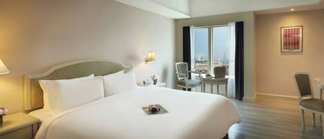 Ein Hotelzimmer mit einem großen Bett, einem Schreibtisch, einem Sessel und Blick auf die Stadt.