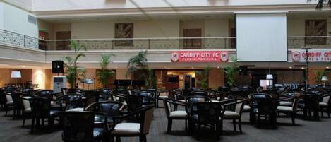 Ampio spazio interno con file di sedie e tavoli, un cartello del Cardiff City FC e un balcone con piante.