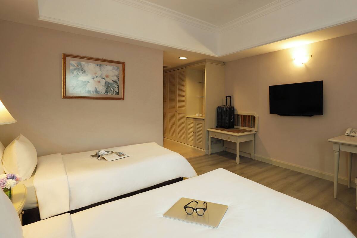 A hotel room with two beds, a desk, a TV, and a painting on the wall.