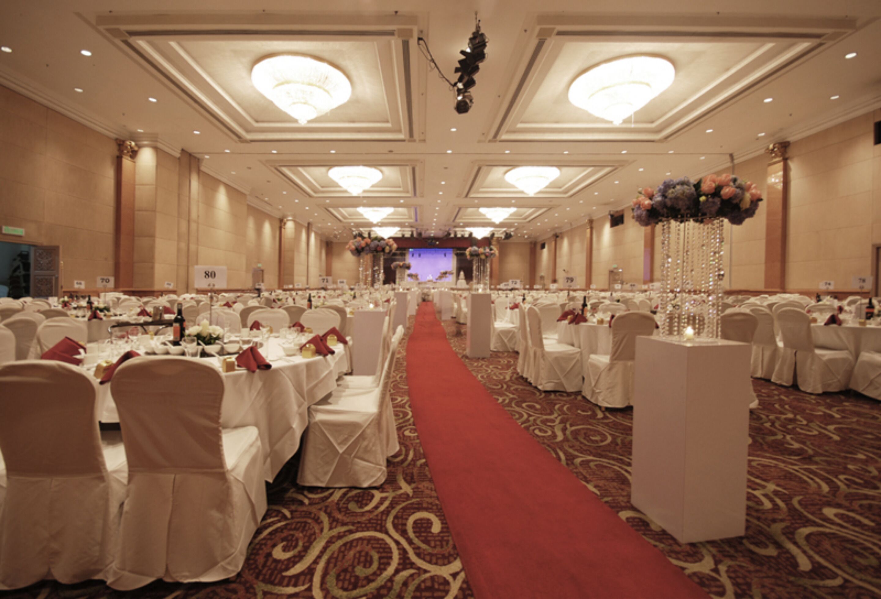 A banquet hall with rows of round tables, white tablecloths, and red carpeted aisle.