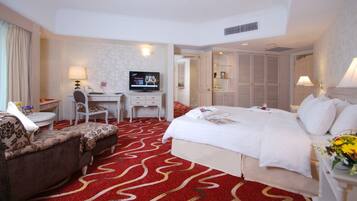A hotel room with a large bed, a desk with a TV, a chair, and a red carpet.