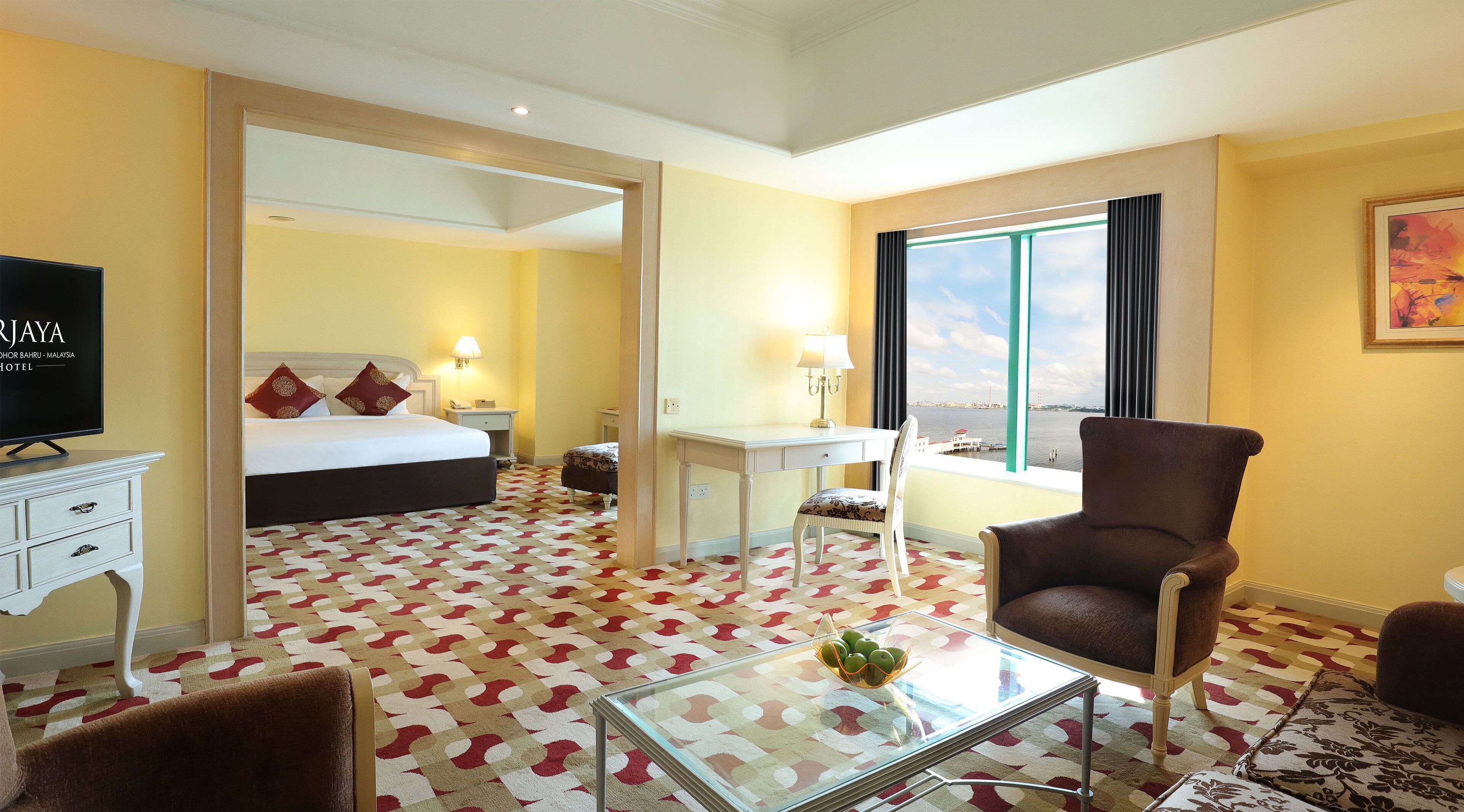 A hotel room with a bed, a desk, a chair, a TV, and a view of the water.