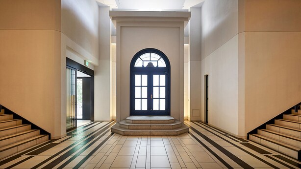 Un hall d’entrée spacieux, doté d’une grande porte en arc, avec un escalier sur la gauche et un autre sur la droite.
