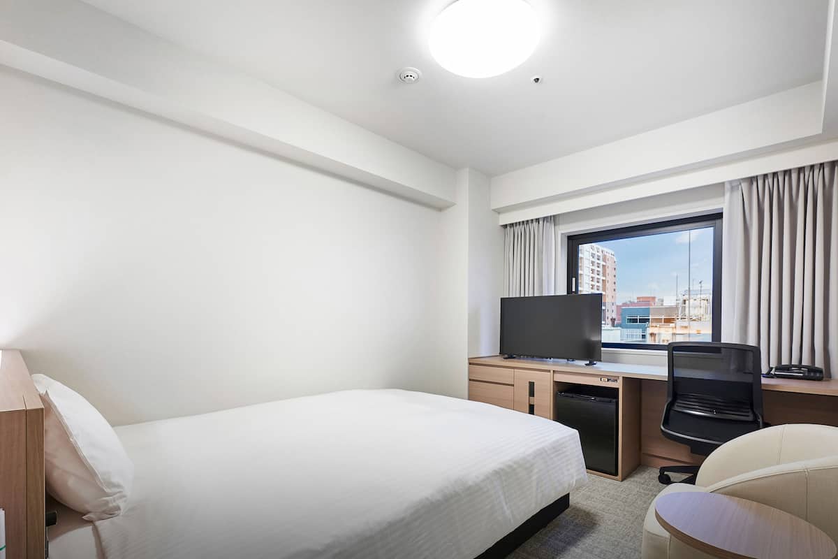 Une chambre d’hôtel équipée d’un lit, d’un bureau, d’une chaise, d’une télévision et offrant une vue sur les bâtiments par la fenêtre.