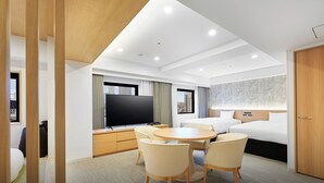 Une chambre d’hôtel moderne dotée d’un coin repas, d’un grand téléviseur à écran plat, d’un lit avec une tête de lit et offrant une vue sur le paysage urbain par la fenêtre.