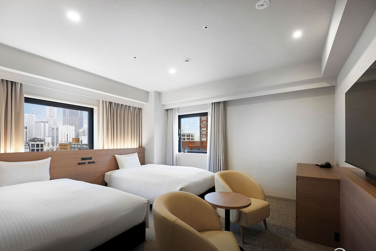 Une chambre d’hôtel avec deux lits, une petite table, deux chaises, un téléviseur et une vue sur la ville.