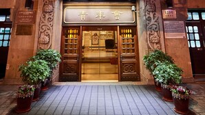 A hotel entrance with ornate architectural details, a signboard with hotel name, and potted plants at the entrance. - Jinjiang Metropolo Hotel Classiq, YMCA (Shanghai)