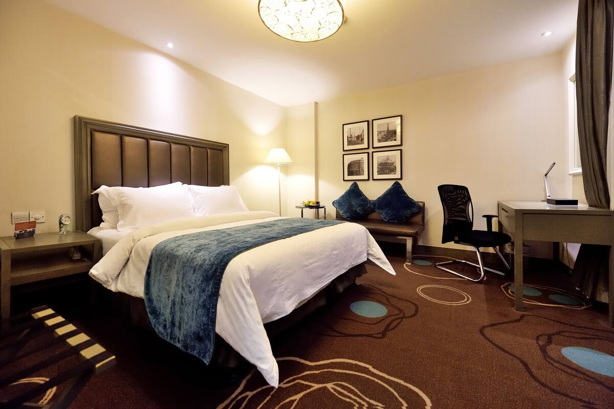 A hotel room with a bed, bedside table, lamp, chair, desk, and framed pictures on the wall.