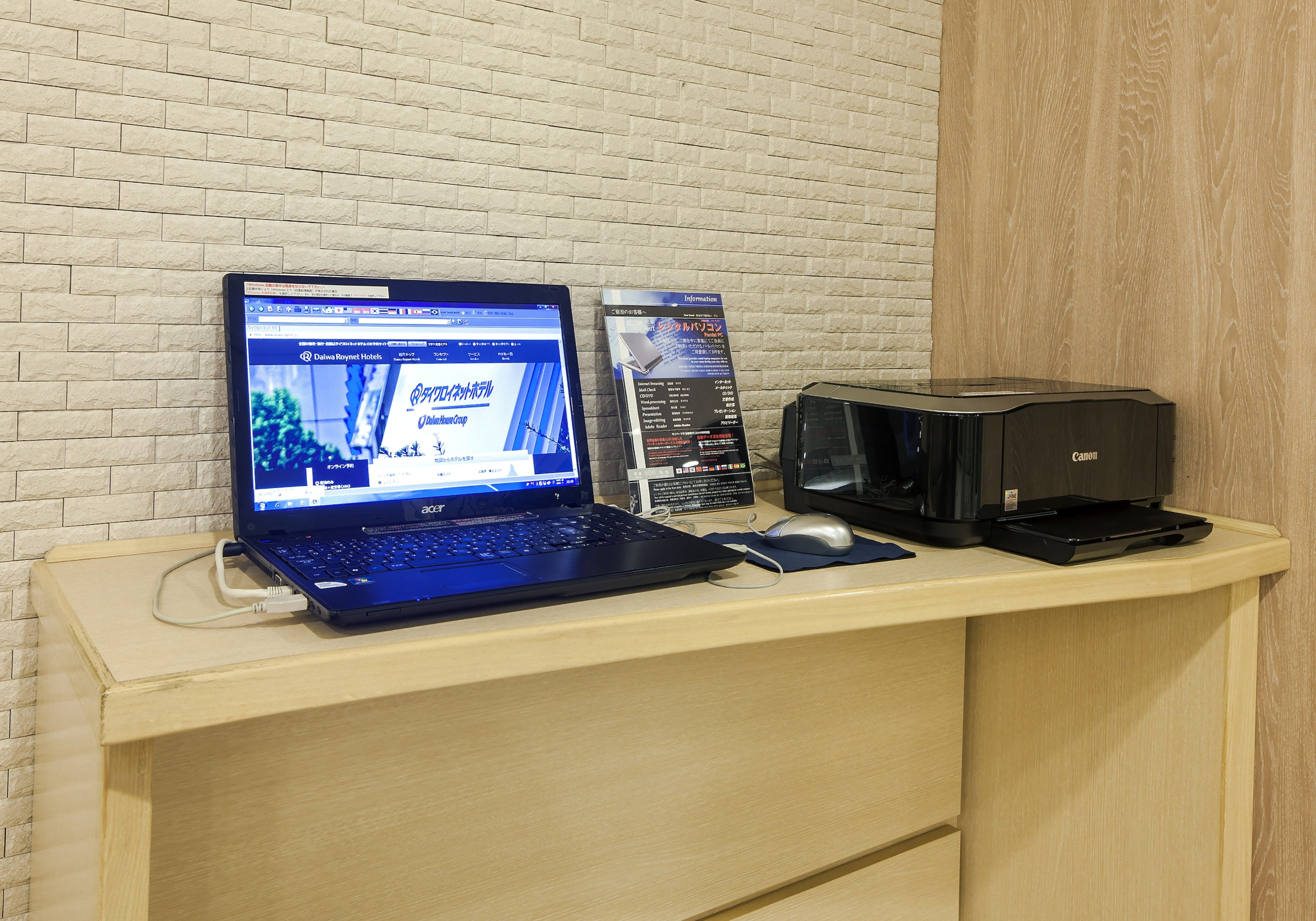 A laptop on a desk with a printer and a sign.