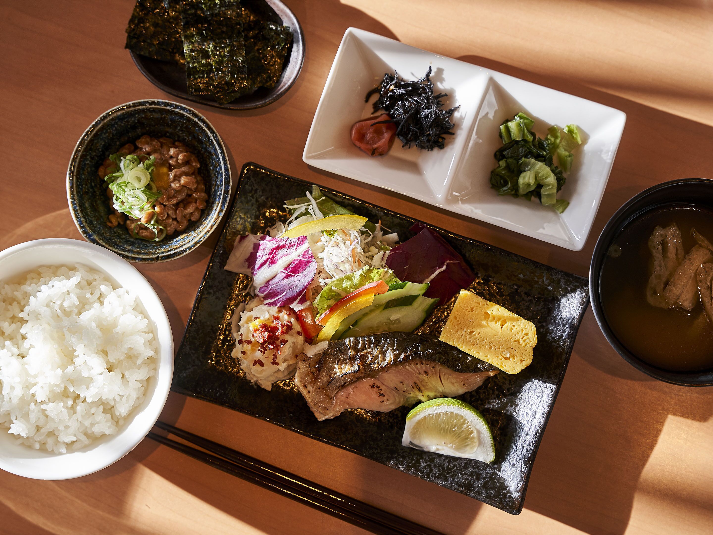 A variety of dishes including rice, meat, and vegetables on a black plate, with side dishes of seaweed, salad, and soup.