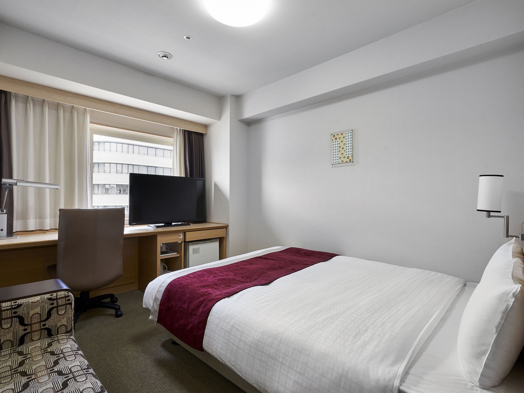 Een hotelkamer met een bed, een bureau met een televisie, een stoel en een lamp.