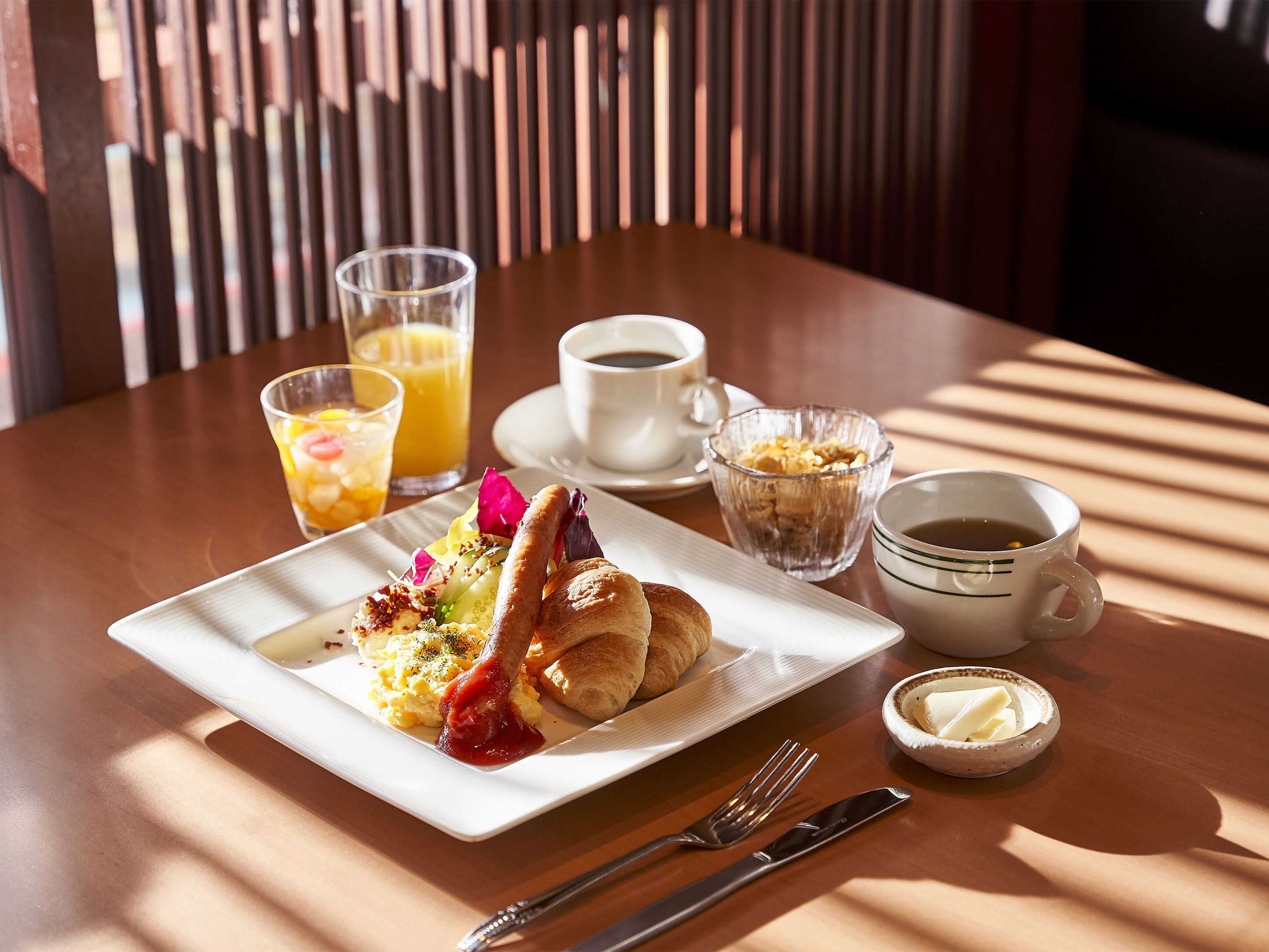 A breakfast setting with a plate of food, a glass of orange juice, a cup of coffee, and a bowl of butter.