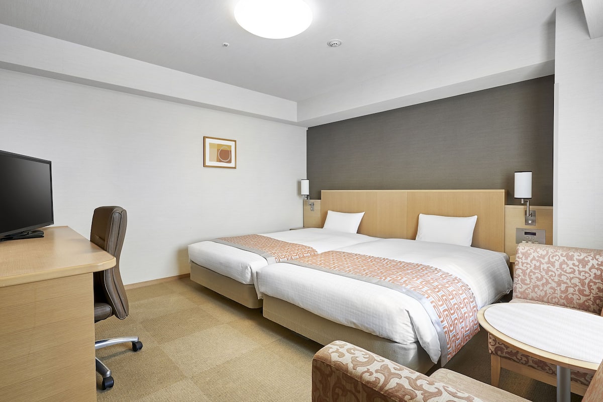 A hotel room with a bed, a desk, a chair, and a small table.