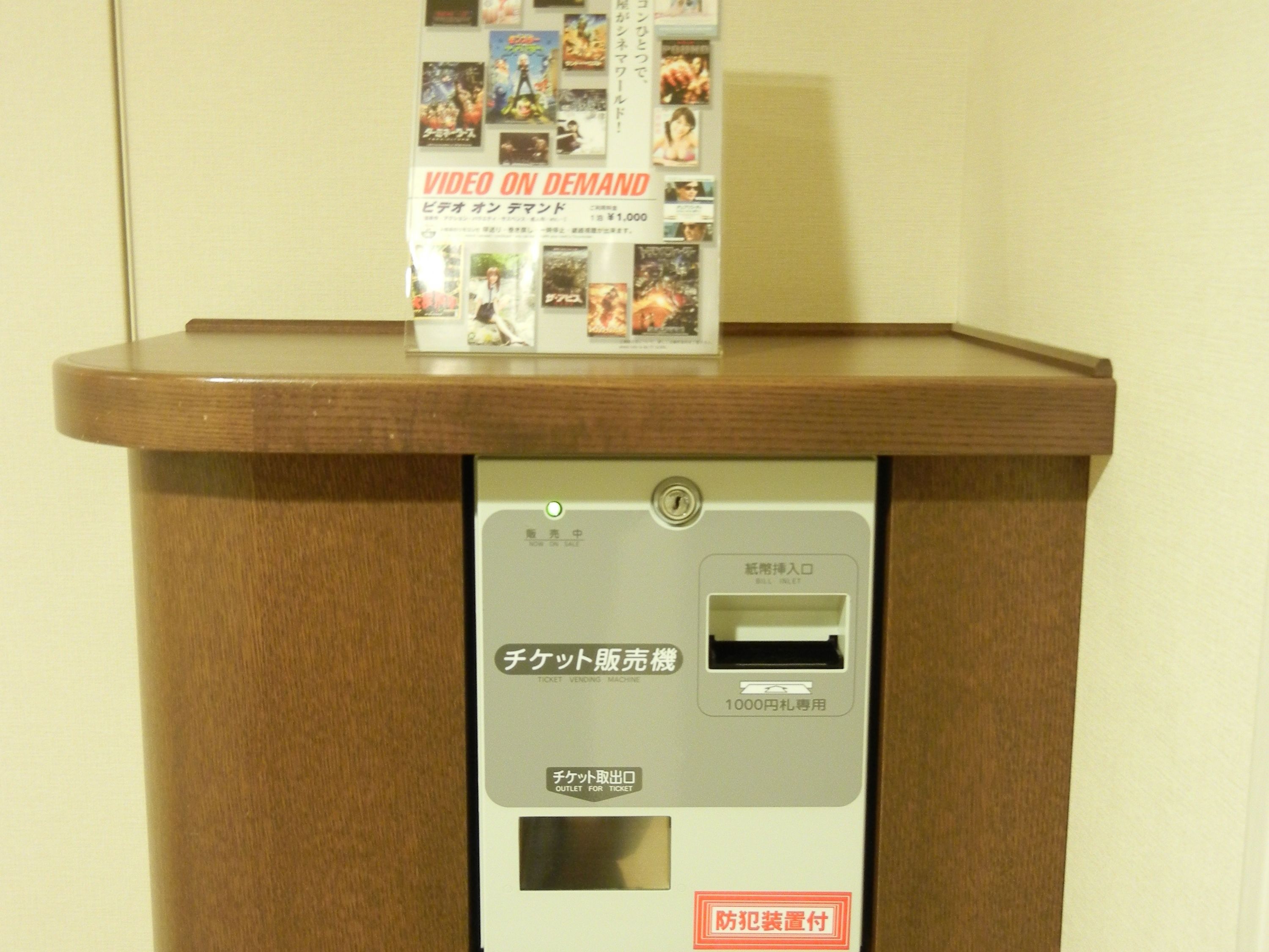 A ticket vending machine with a wooden counter and a poster advertising video on demand.