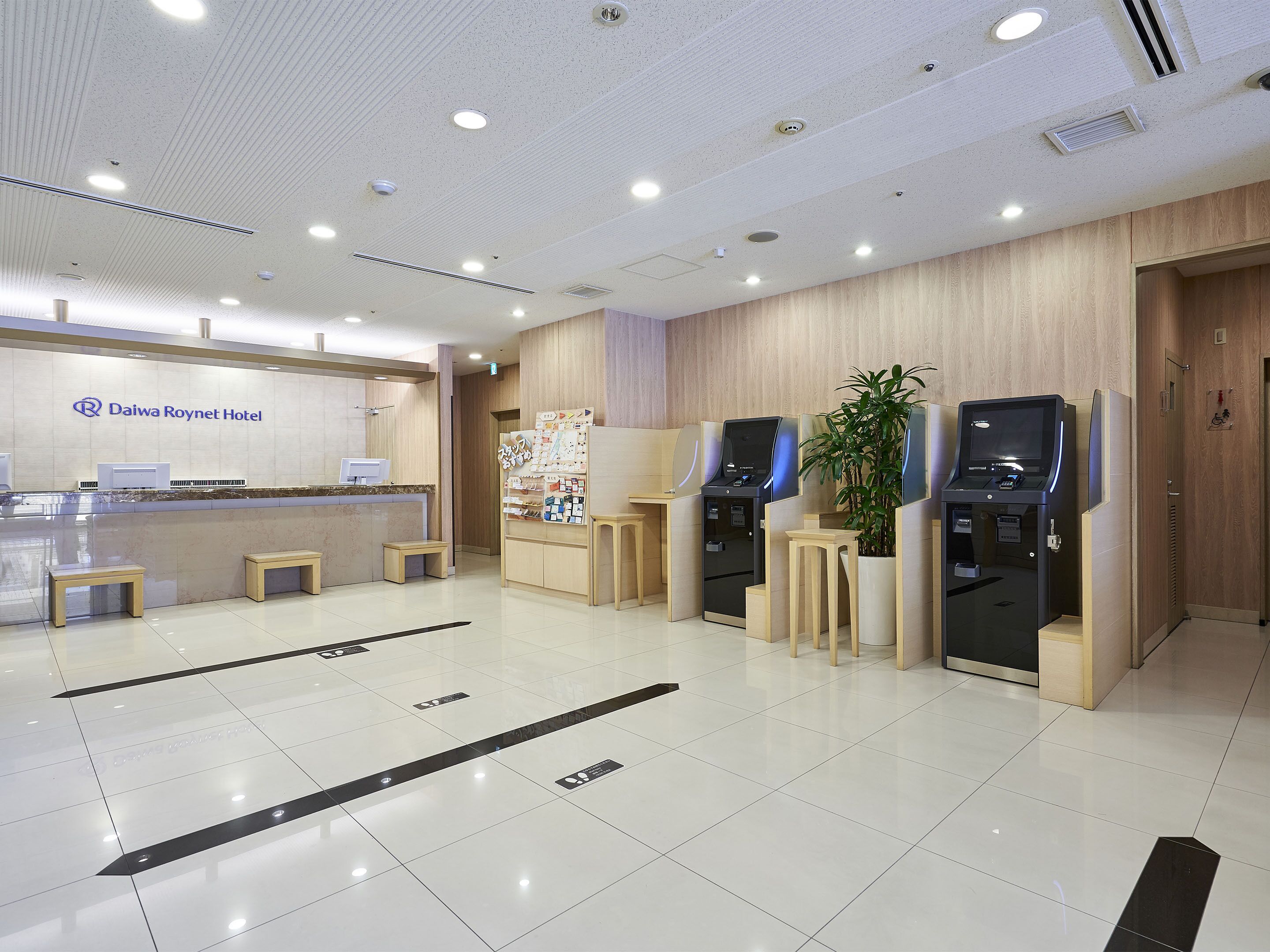 Zona de recepción de hotel con mostrador, asientos y quioscos de autoservicio.