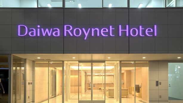 Indgangen til Daiwa Roynet Hotel med en glasfacade og oplyst skiltning.