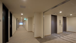 Et hotel med et tæppe beklædt gulv, døre på begge sider samt en synlig elevator.