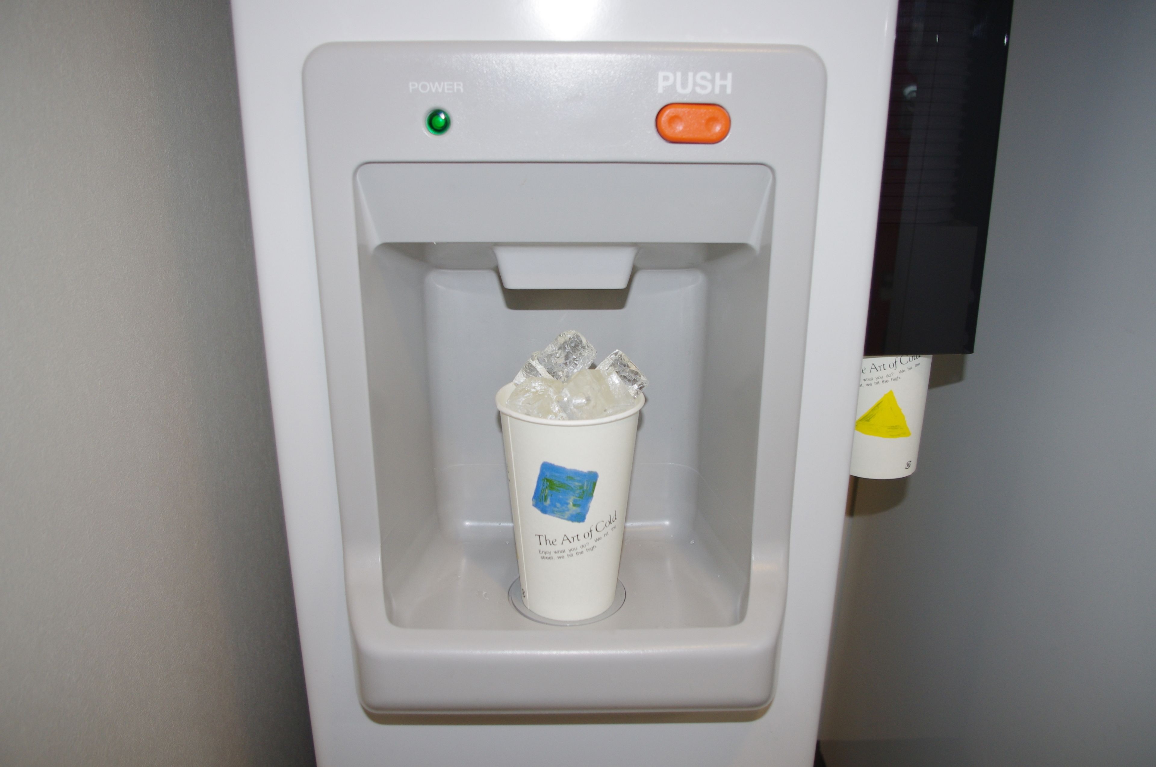 A water dispenser with a cup containing ice cubes.