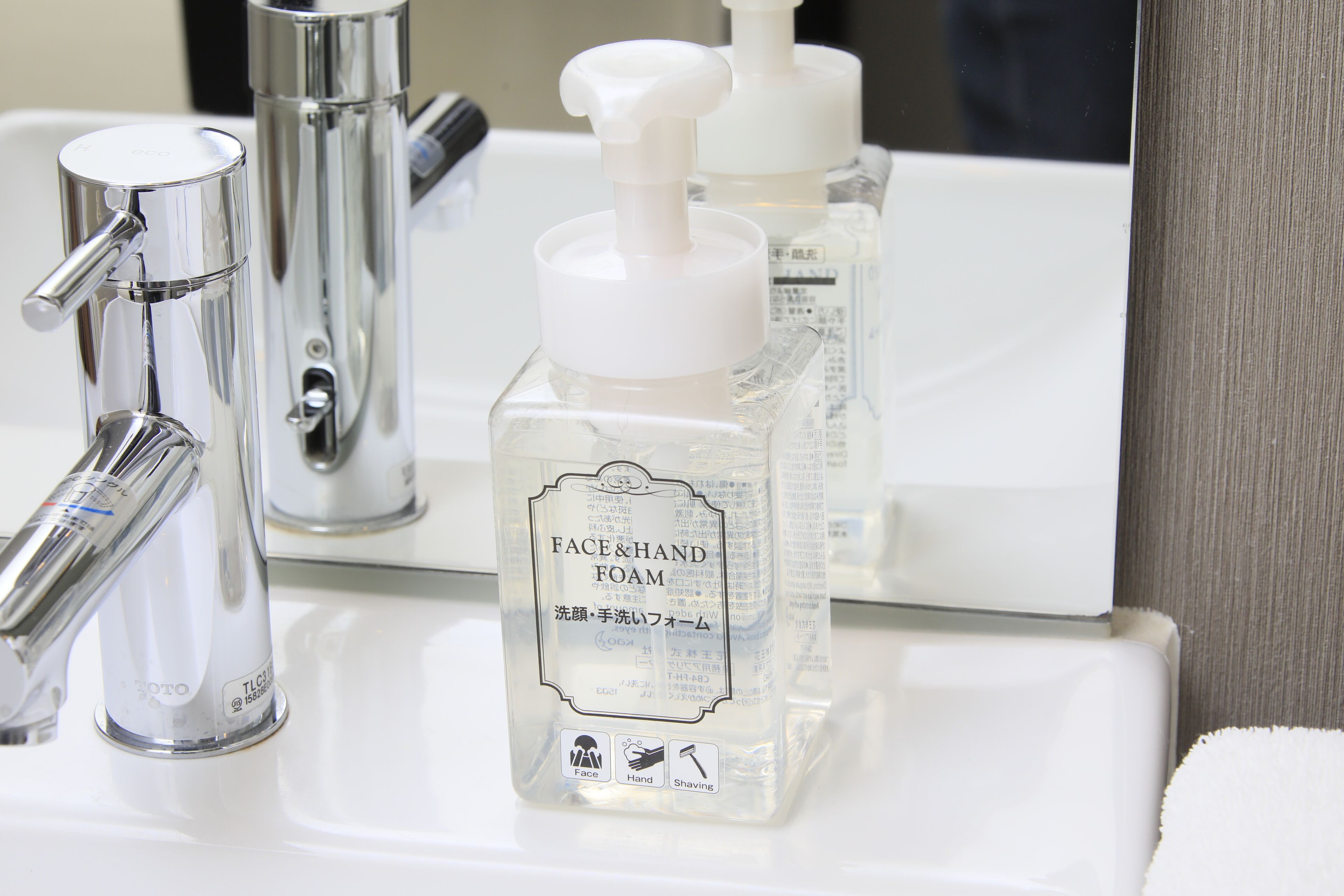 Un lavabo de salle de bain avec un robinet chromé et un flacon de mousse nettoyante pour le visage et les mains.