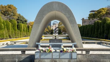 Monumento de piedra con inscripciones y arreglos florales en un parque ajardinado.