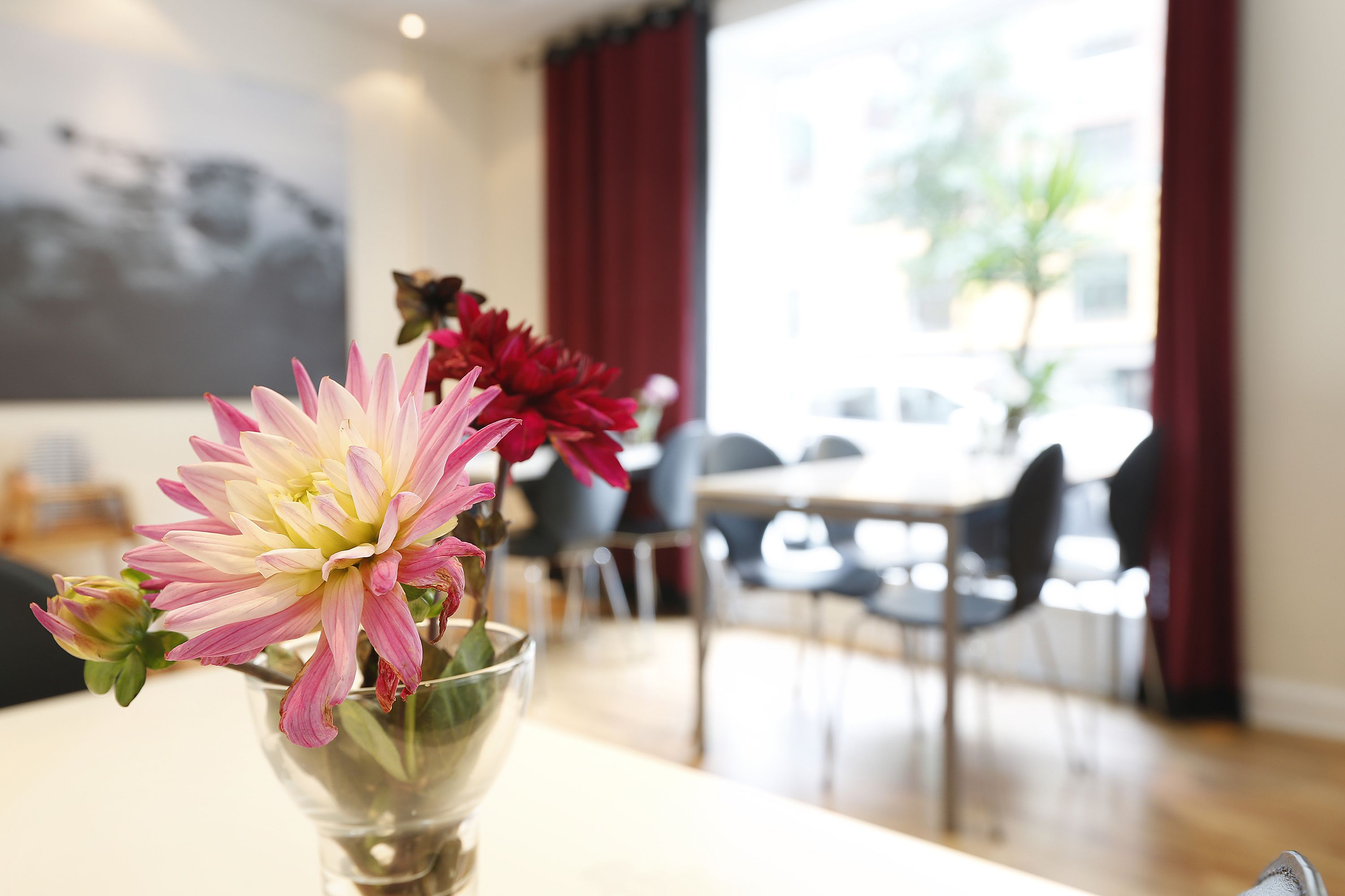 A dining area with a table and chairs, a vase with flowers, and a painting on the wall.