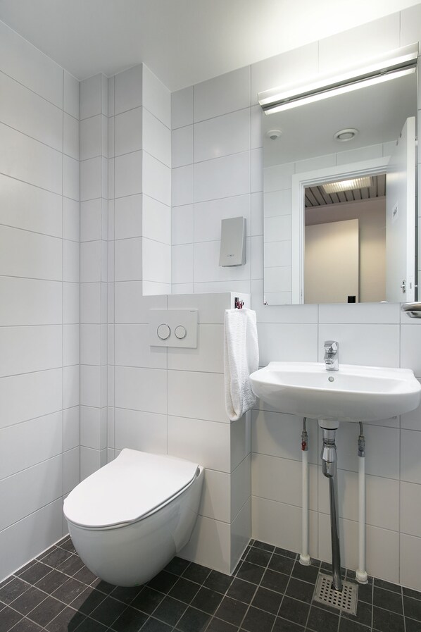 Un baño moderno con azulejos blancos, un inodoro blanco, un lavabo con espejo y una toalla colgada en la pared.