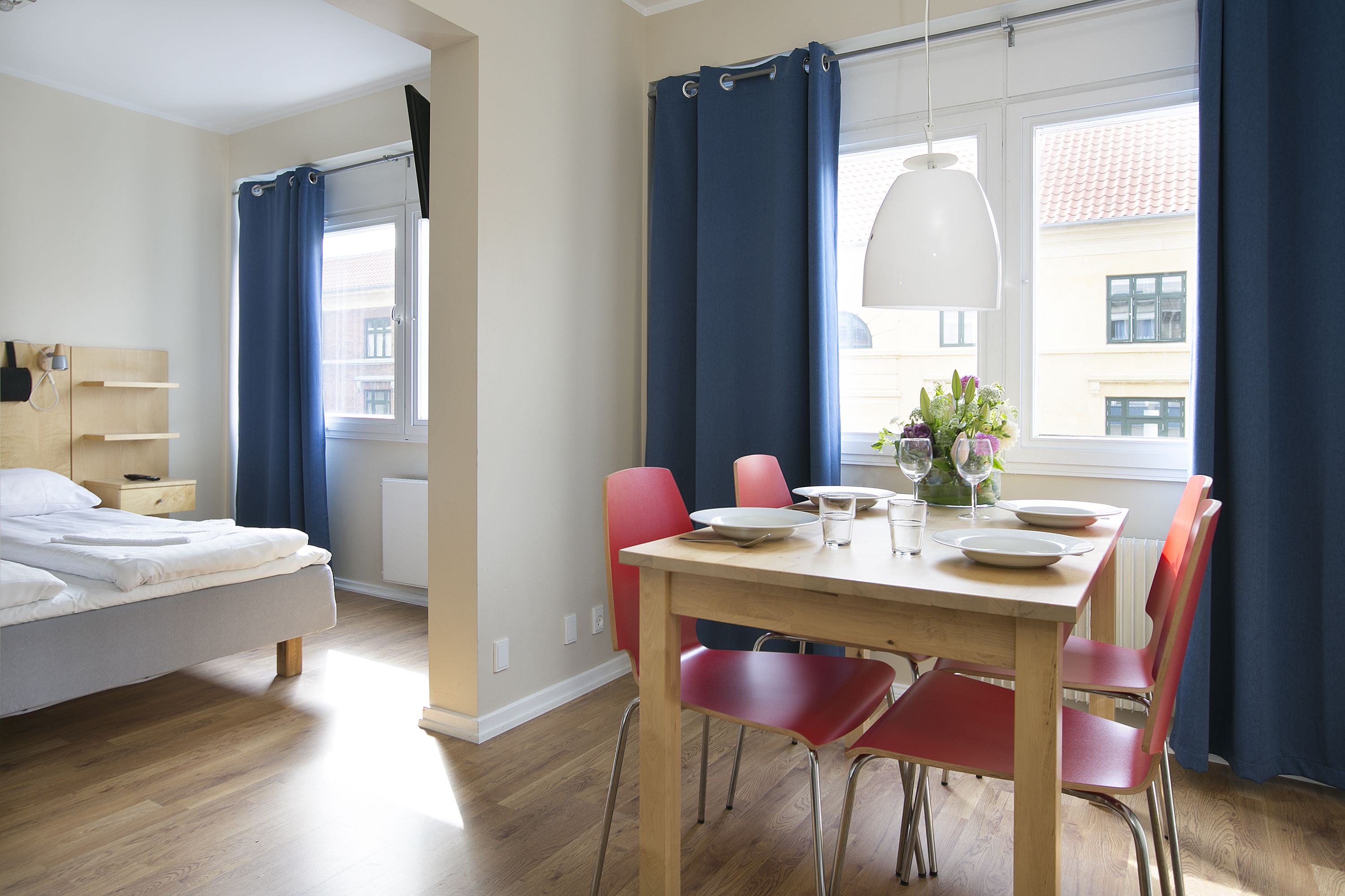 A modern hotel room with a bed, a dining table with chairs, and a window with curtains.