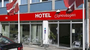 A hotel with a red sign, outdoor seating, and a parked car.