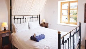 Ein Bett mit Baldachin, Nachttische mit Lampen, ein Fenster mit Aussicht und eine Holzbalkendecke.