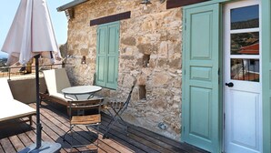 Ein Steinhaus mit einer Holzdielenveranda, Sitzgelegenheiten im Freien und einer Tür mit Fenster.