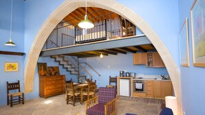 Ein geräumiger Wohnbereich mit hoher Decke, einer Treppe zu einer oberen Ebene, einem Essbereich mit Holzzmöbeln und einer Küche mit Holzausstattung.