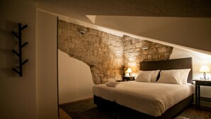 Un dormitorio con pared de piedra, una cama, una mesita de noche con lámpara y un perchero.