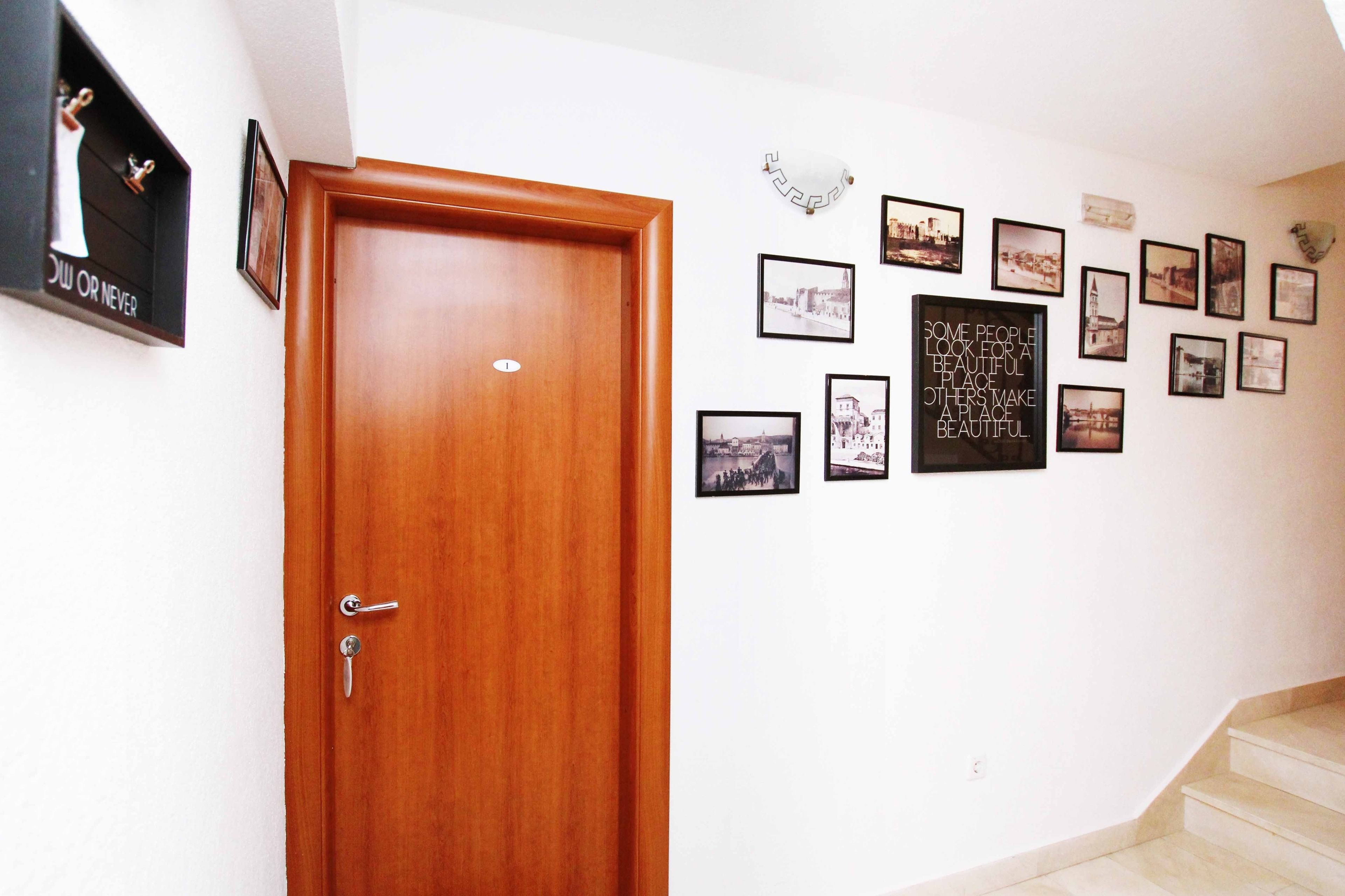 A hallway with a wooden door, a coat rack, and a wall decorated with framed pictures and a motivational quote.