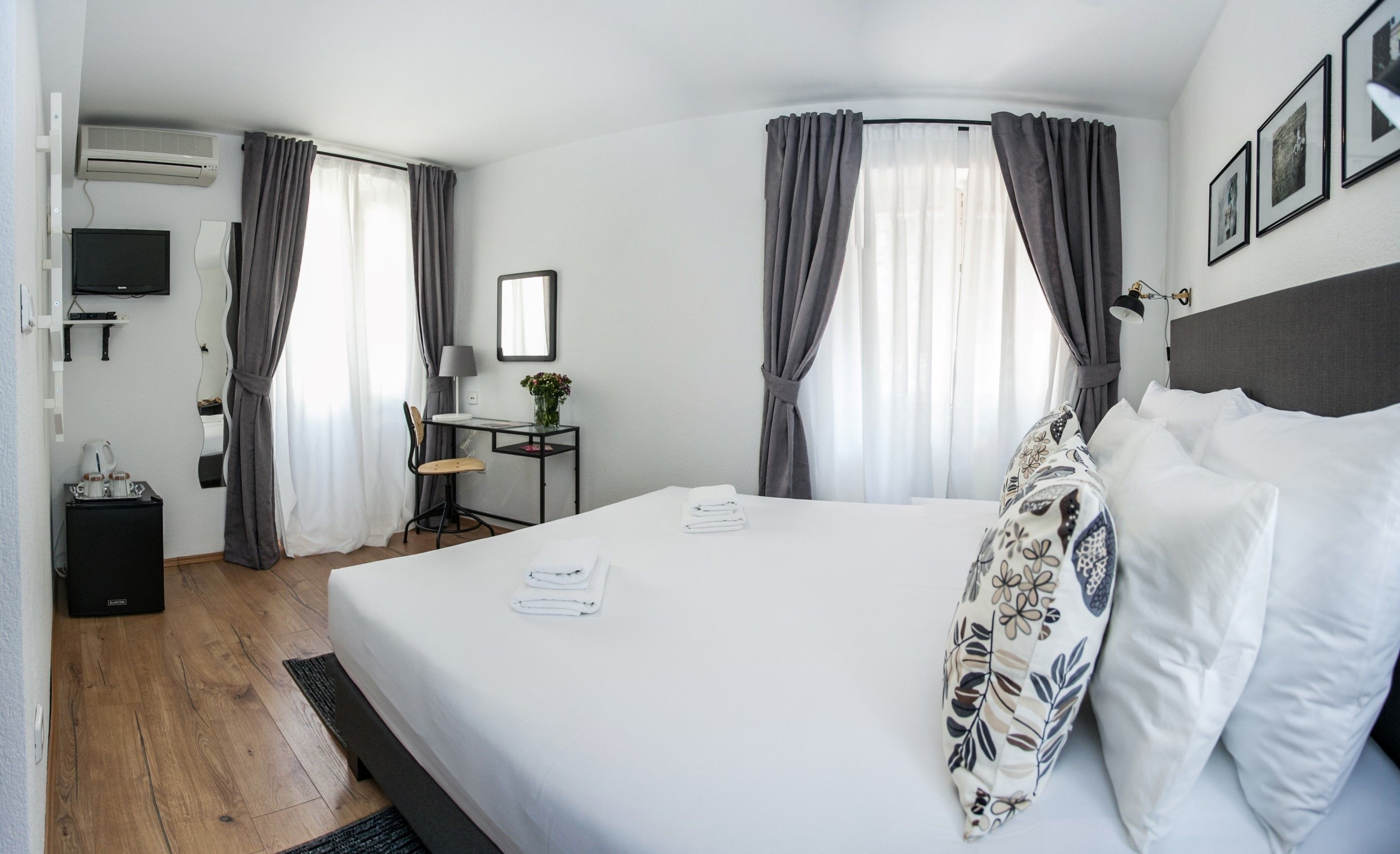 A hotel room with a bed, a desk, a chair, a TV, and a window with curtains.
