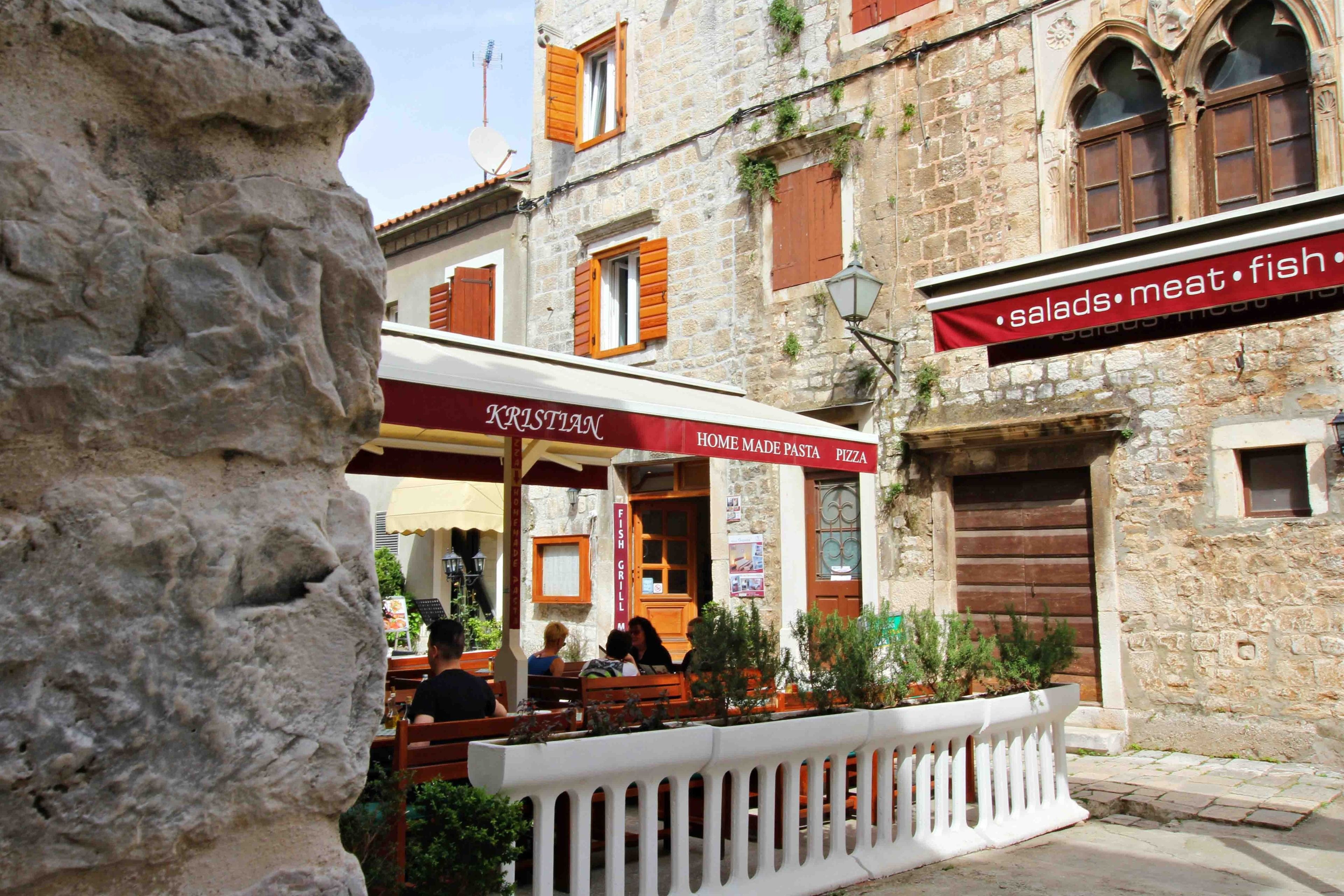 Un edificio de piedra con un restaurante llamado 'KRISTIAN' que sirve pasta y pizza.