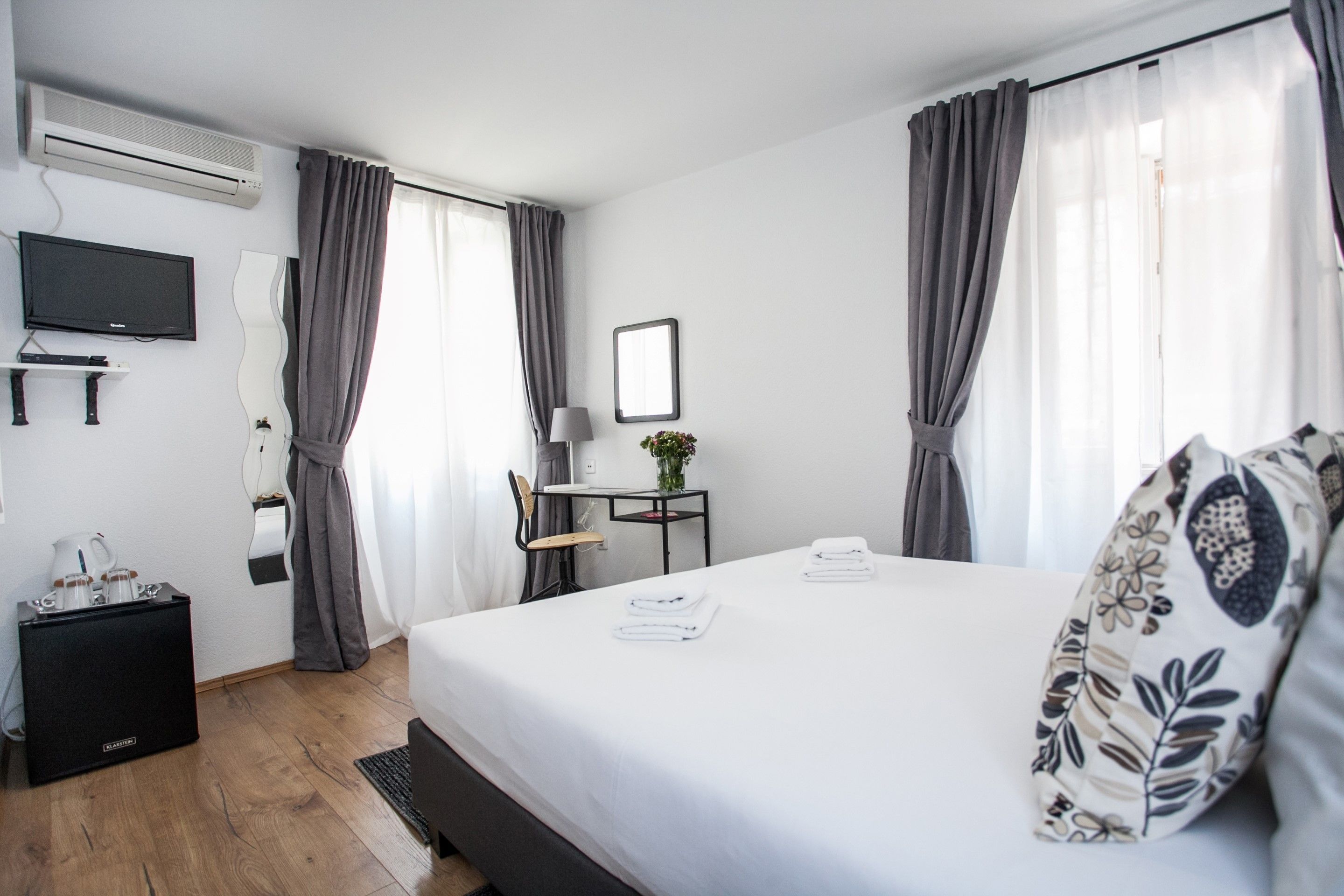 Een hotelkamer met een bed, een televisie, een bureau met een lamp en een kleine tafel met een plant.