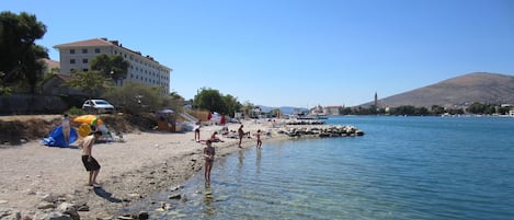 A beach with clear water, rocky shore, and a building in the background.