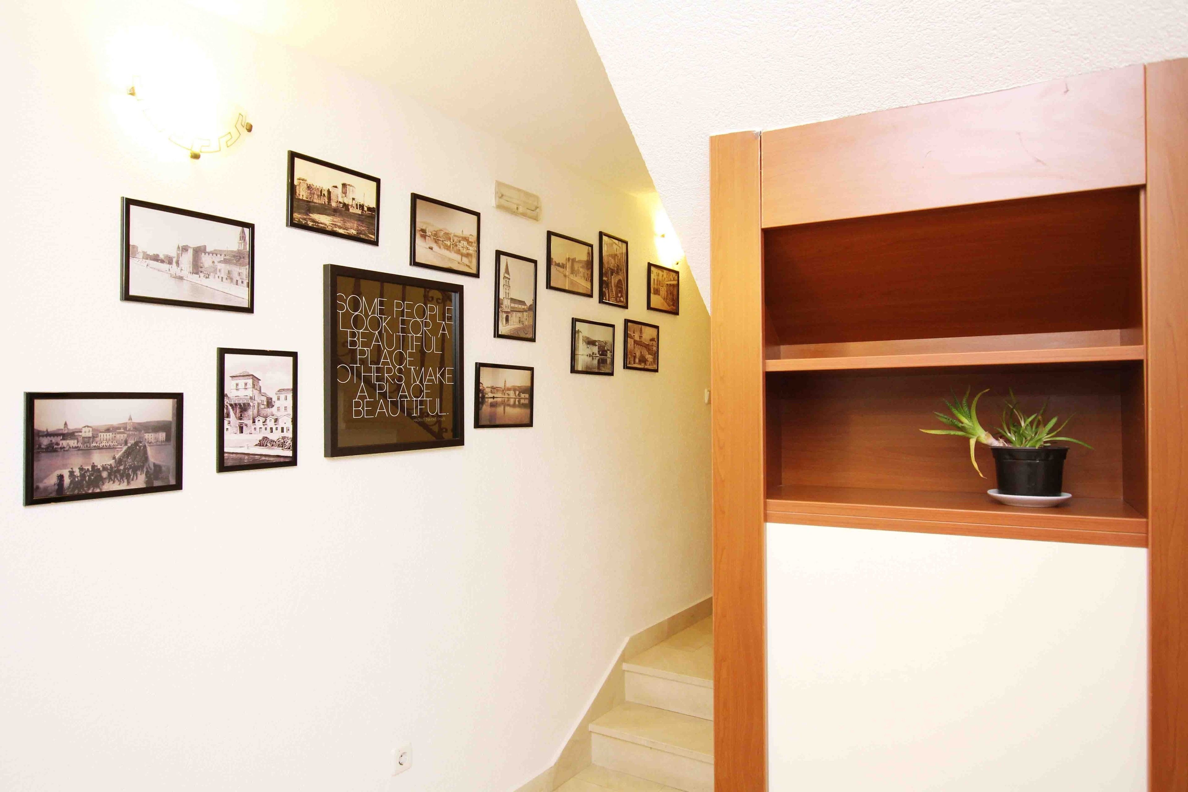 A hallway with a series of framed photographs on the wall, a wooden cabinet with a plant, and a staircase.