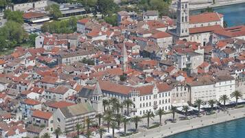 Vista aérea de un pueblo histórico con edificios apretados, una iglesia destacada con una torre alta y un paseo marítimo con palmeras.